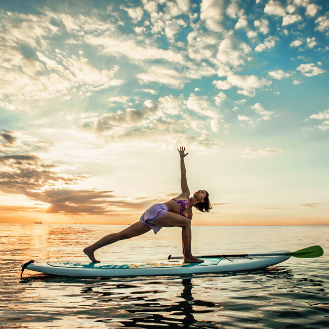 young woman doing yoga on a sup board in the lake BBVVTFX